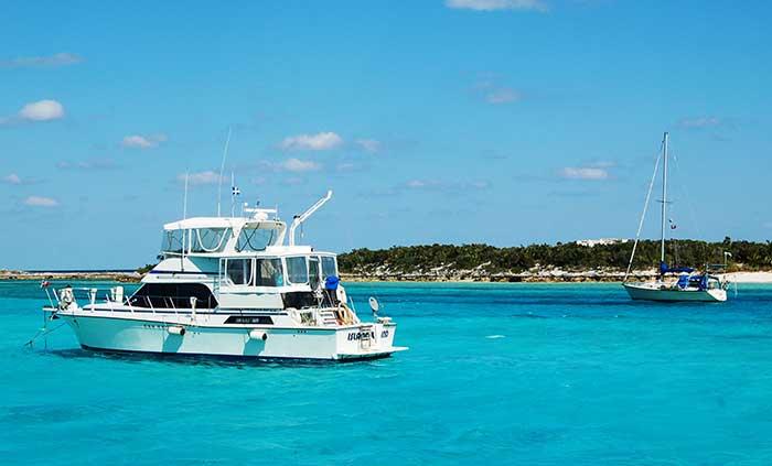 A large motoryacht and a sailboat are anchored near one another in clear blue, teal water.
