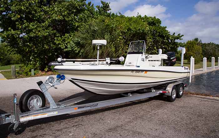 Medium sized white and light yellow boat sitting on its trailer at the waters edge of a boat ramp
