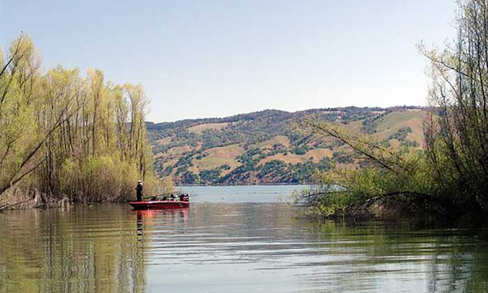 Man standing on bow of a small red boat in the distance on Clear Lake