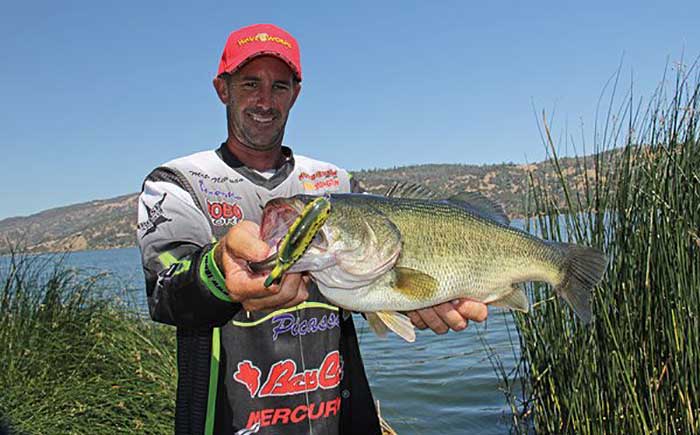 Man wearing a red ball cap fishing competition jersey standing holding large bass catch
