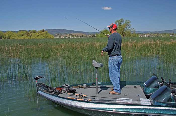 Man standing on bow of small boat holding a fishing rod in the shallows of Clear Lake