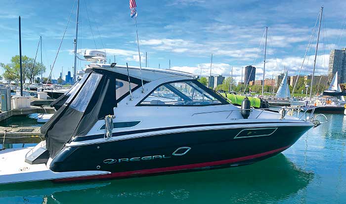 Blue and white Regal 35 Sport Coup powerboat docked at a marina with other powerboats, sailboats and a city skyline in the background