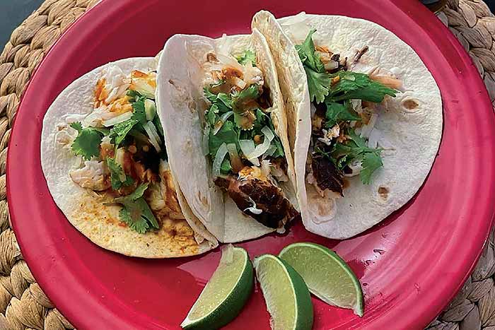 Three snakehead fish tacos open-face, sitting on a pink plate with 3 lime slices as garnish