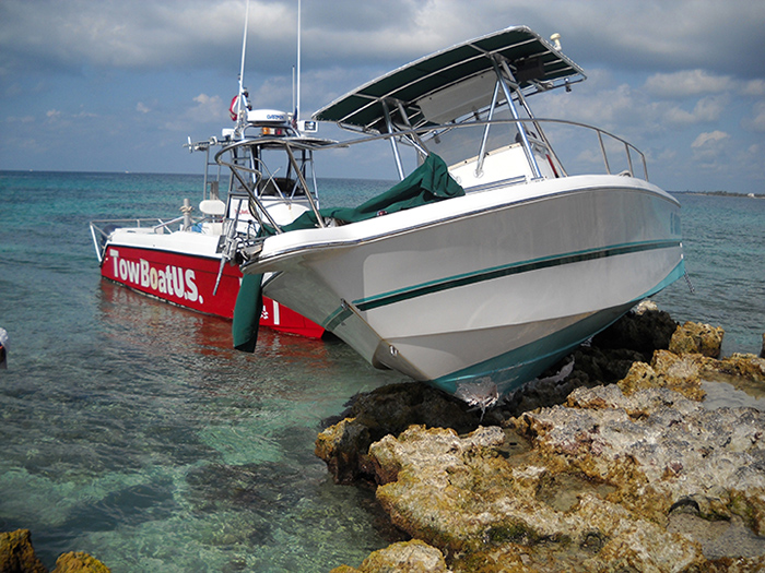 Red and white TowBoatU.S. vessel assisting a white and blue boat on top of rocks.