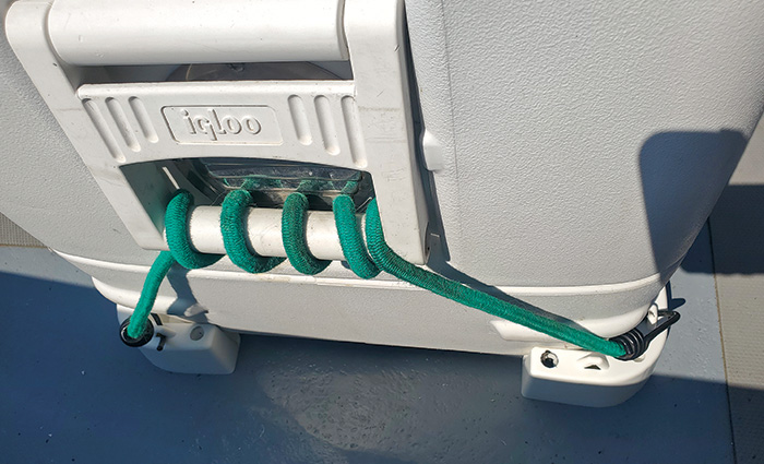 A white cooler being held down by chocks and a green bungee cord.