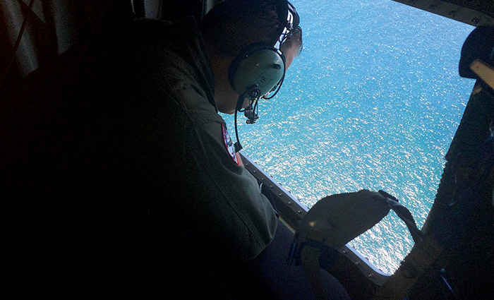 Adult male wearing headphones and peering out of a helicopter down on blue waters during a rescue mission.