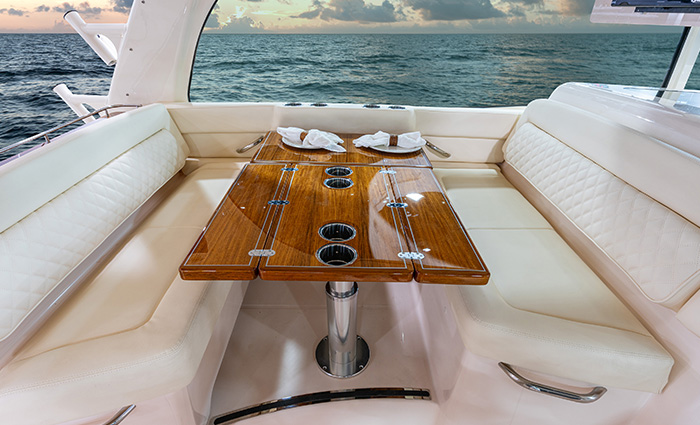 White leather sitting area separated by glossy wooden table on a vessel during sunset.
