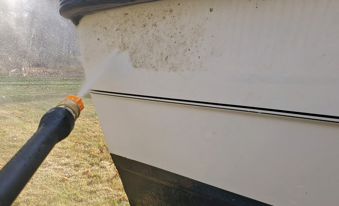Close up photo of the side of a white and black boat being power washed.