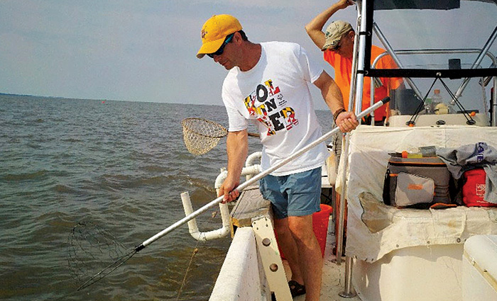 Adult male wearing a yellow hat, white shirt and shorts using a pvc stick as a trotline