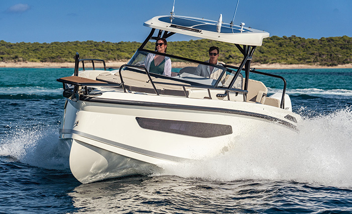 Two young adults navigating a large white vessel on open waters on a sunny day.