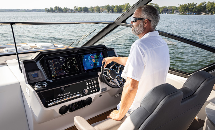 Adult male with gray hair and gray beard wearing sunglasses and a white shirt navigating a vessel out on the water.