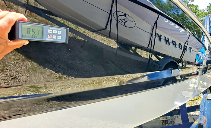 Glossmeter held next to a black boat displaying an 85.1 after ceramic application.