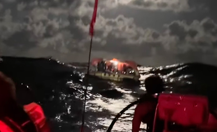 Numerous passengers awaiting help aboard a sinking vessel on open waters at night.