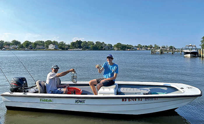 Two adults in a white fishing boat proudly showing off crabs caught out on the water on a sunny day.