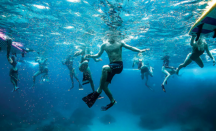 Underwater view of several adults swimming and using various water toys.