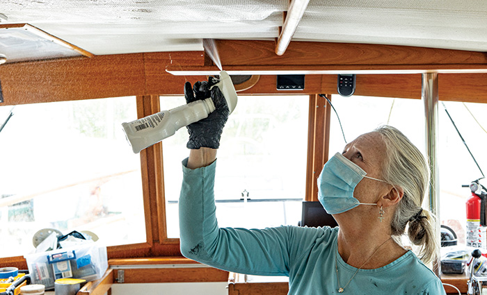Senior female wearing a blue mask cleaning spraying the overhead of a vessel.
