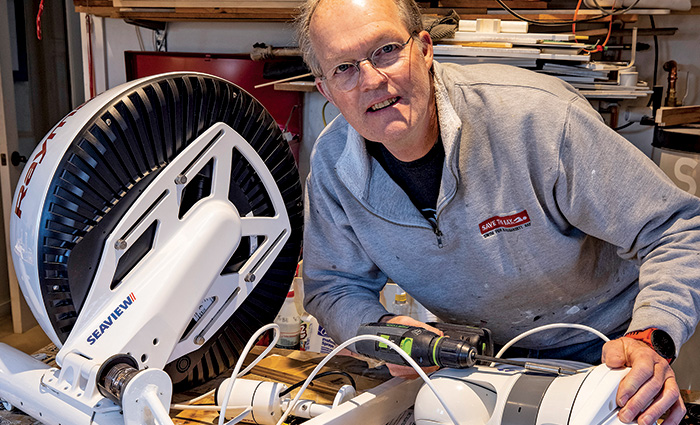 Senior male wearing glasses and a gray pullover posing for a photo as his work bench.