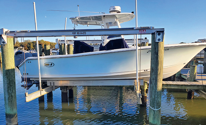 Side view of a white vessel with navy seats on a lift at a wooden dock on a clear day.