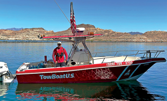 Adult male wearing a red jacket and white hat aboard a red TowBoatU.S. boat out on the water.