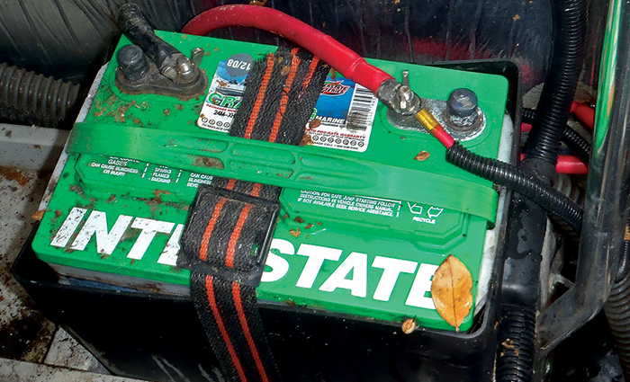 Large green interstate battery held down by a black and red strap.