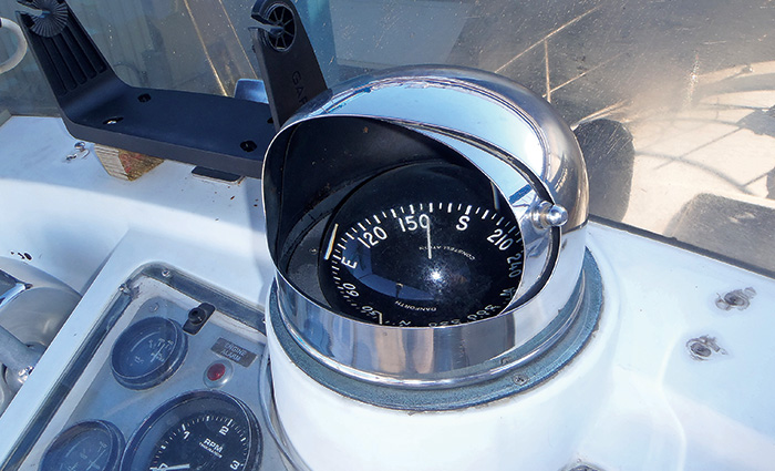 A black boat compass with white numbers and letters shielded from sunlight by a silver covering.
