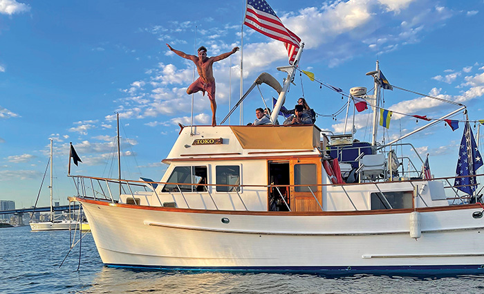 Adult male jumping off a white boat into clear waters on a sunny day.
