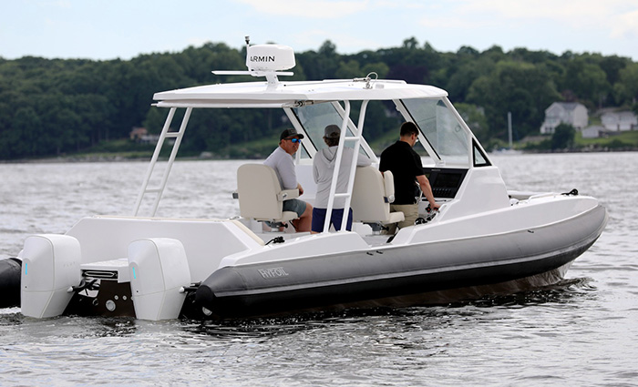 Three adult males aboard a dual engine white vessel out on a lake.