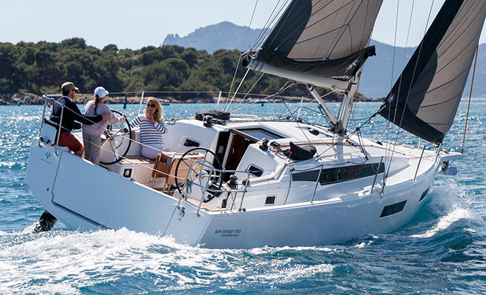 Young female with the help of an adult male steering a large white sailboat with blue and gray sails on open waters.