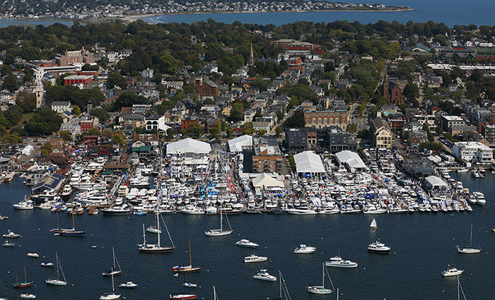 Ariel view of a harbor on a sunny day with numerous boats off the shore on the water.