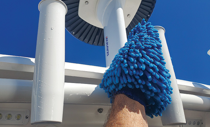 A hand inside of a blue wash mitt cleaning the exterior of a white vessel.