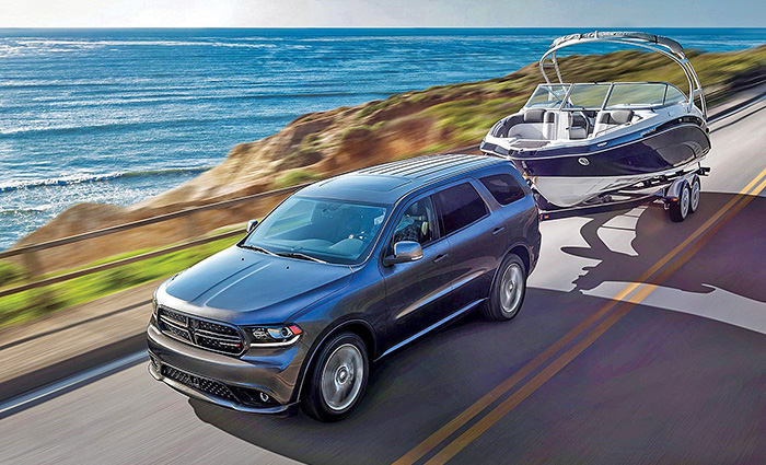 Large black SUV towing a white and navy boat on a highway alongside the coastline.