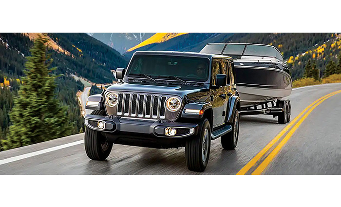 A black jeep hauling a white and navy boat on a mountainside road.
