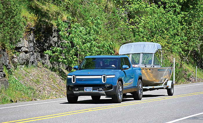 A blue truck towing a silver boat along a road.