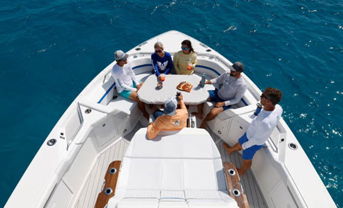 Aerial view of six adults sitting around a white table aboard a white vessel out at sea.