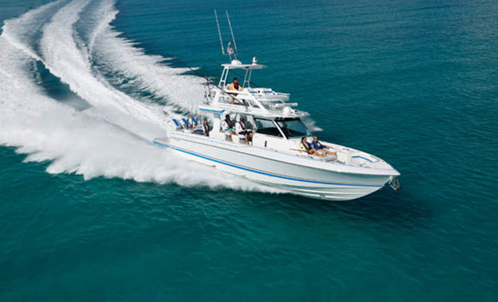 Aerial view of a white vessel with light blue stripe cruising through open waters on a sunny day. 