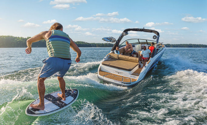 Adult male wakeboarding during a sunny day while being pulled by a white and black Sea Ray.