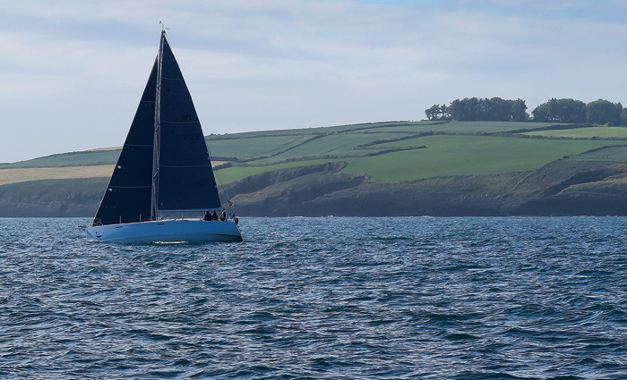 White sailboat with navy sails on dark blue waters off the coast of bright green land.