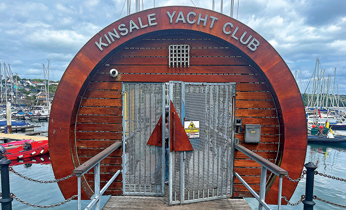 Circular burnt red wooden entrance with metal gates leading to a dock and numerous sailboats.