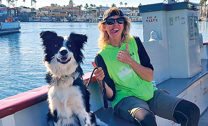 Female wearing sunglasses and a lime green shirt with her tongue out posing for a photo next to a black and white dog.