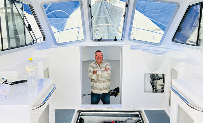 Adult male wearing a stripped long sleeve collared shirt standing in the cabin of a white boat.