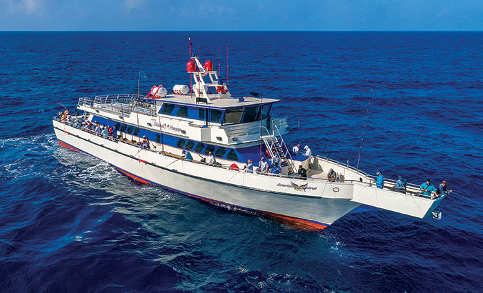 Large white boat with red trim out at sea carrying numerous people fishing.
