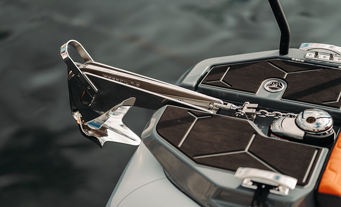 Up-close view of a stainless steel anchor above water in the background.