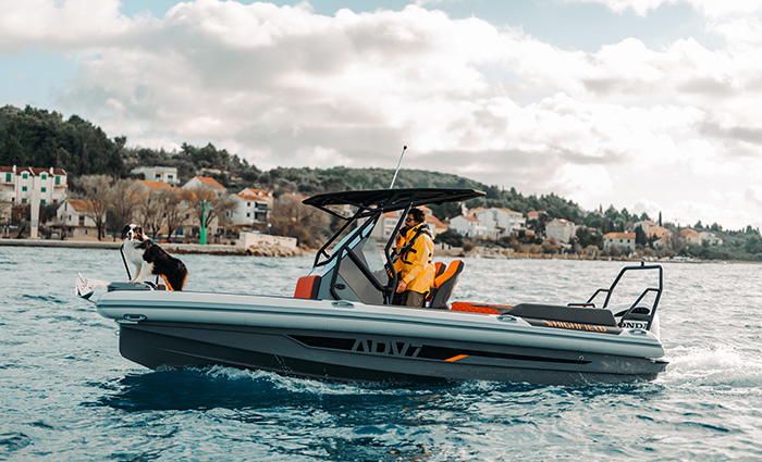 Man and woman wearing orange rain jackets aboard a silver and black fiberglass boat on the water.
