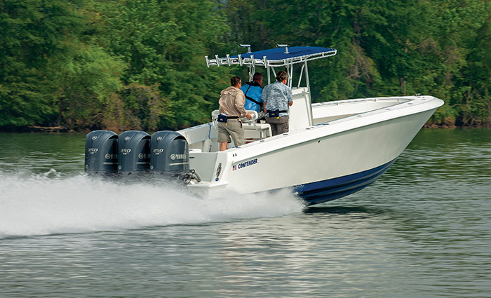Three men in a white and blue boat speeding through open waters with lush trees in the background.