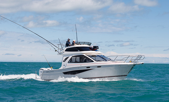 Large white vessel with three large fishing poles out on clear blue open waters.