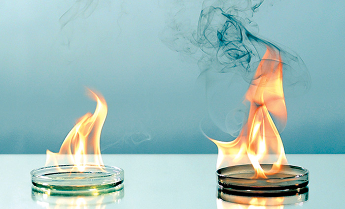 Two small containers with fuel lit demonstrating flames - one with dark smoke.