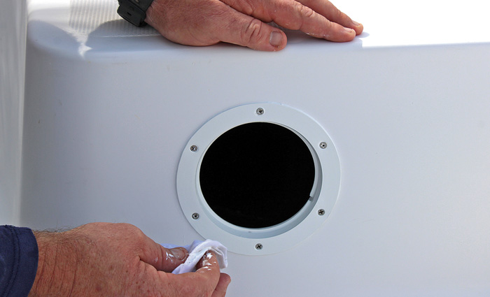 A set of hands applying the finishing touches to a deck plate hole in a white boat.