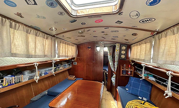 Rehabbed interior cabin of a boat with a white ceiling covered in various stinkers, white curtains  and a long wooden table.