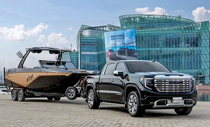 A black four door GMC truck parked beside a dock with a black and gold boat on its trailer.