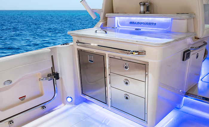 Cockpit of a white vessel out on blue open waters featuring a stainless steel refrigerator, grill, sink and more.